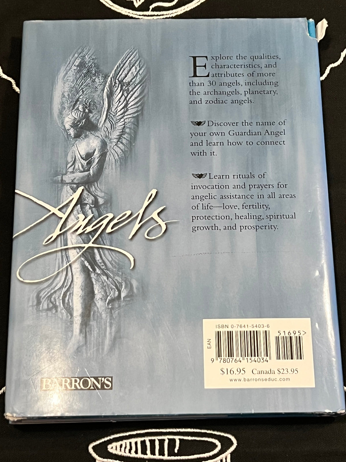 Back cover of a Barron's book titled 'Angels' featuring a light blue-gray background, an illustration of an angel, descriptive text, and a barcode label.
