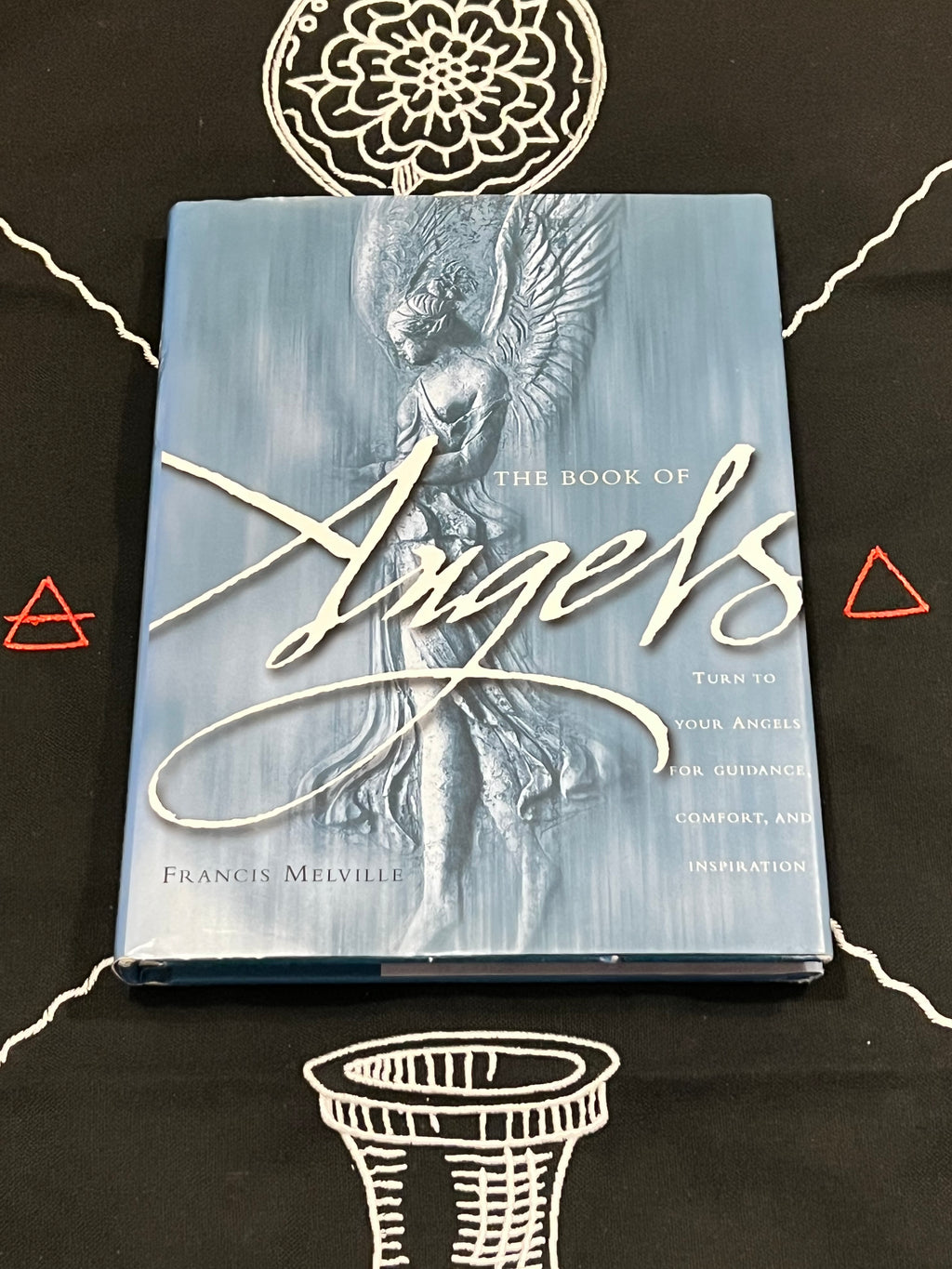 The Book of Angels by Francis Melville, featuring a textured light blue cover with a silver-toned angel statue and elegant white script title, displayed on a black background with white line drawings.