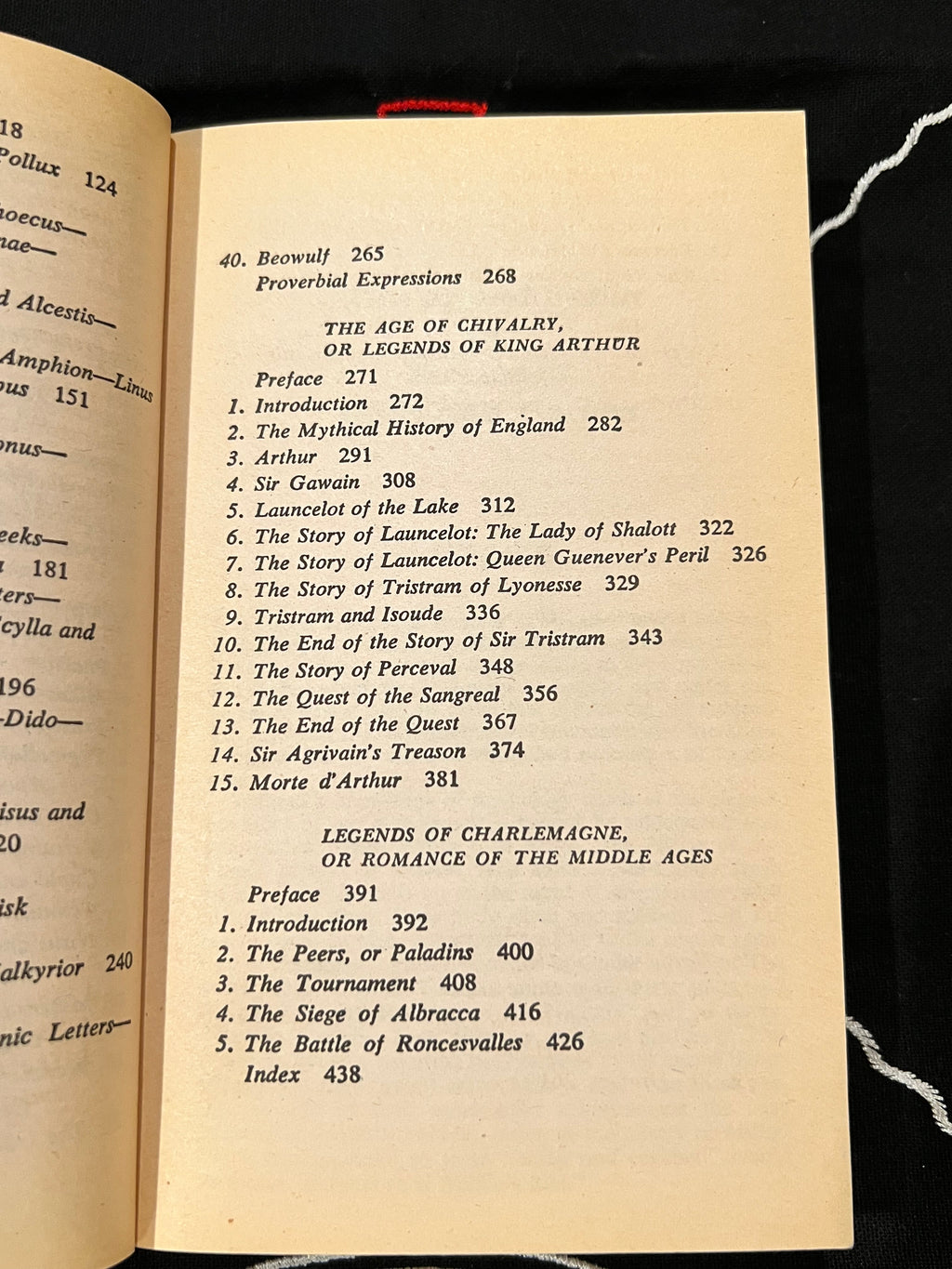 An open book showing printed text and a table of contents on aged cream paper, photographed against a dark fabric background with a white cord visible at the edges.