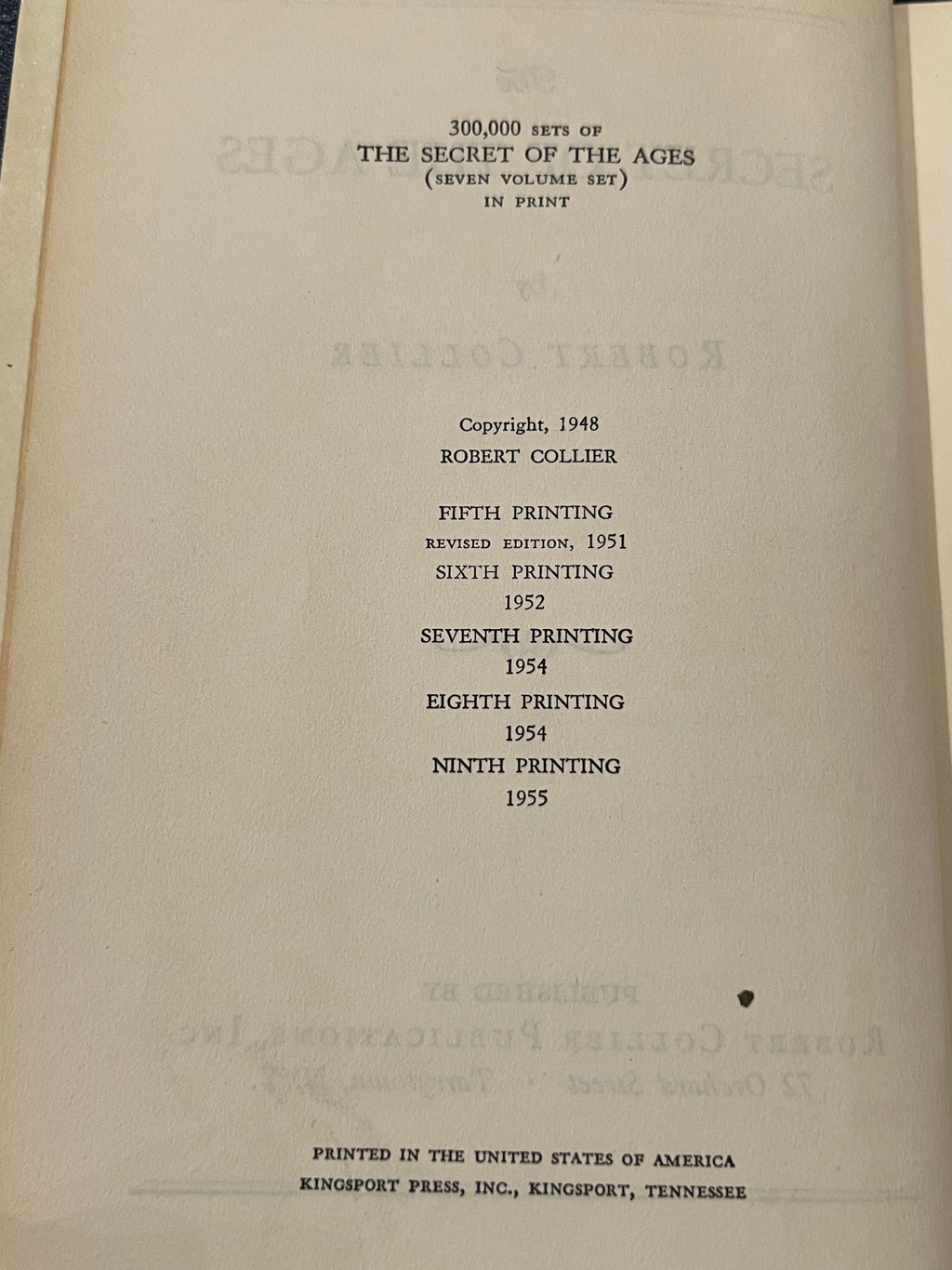 A close-up of an open book's inner page showing printed copyright and printing information for 'The Secret of the Ages' by Robert Collier, with the left page edge and a small portion of a finger visible at the bottom left.