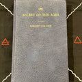 A vintage hardcover book titled 'The Secret of the Ages' by Robert Collier, featuring a textured dark blue-gray cover with gold lettering, displayed on a black background with white line art and red geometric symbols.