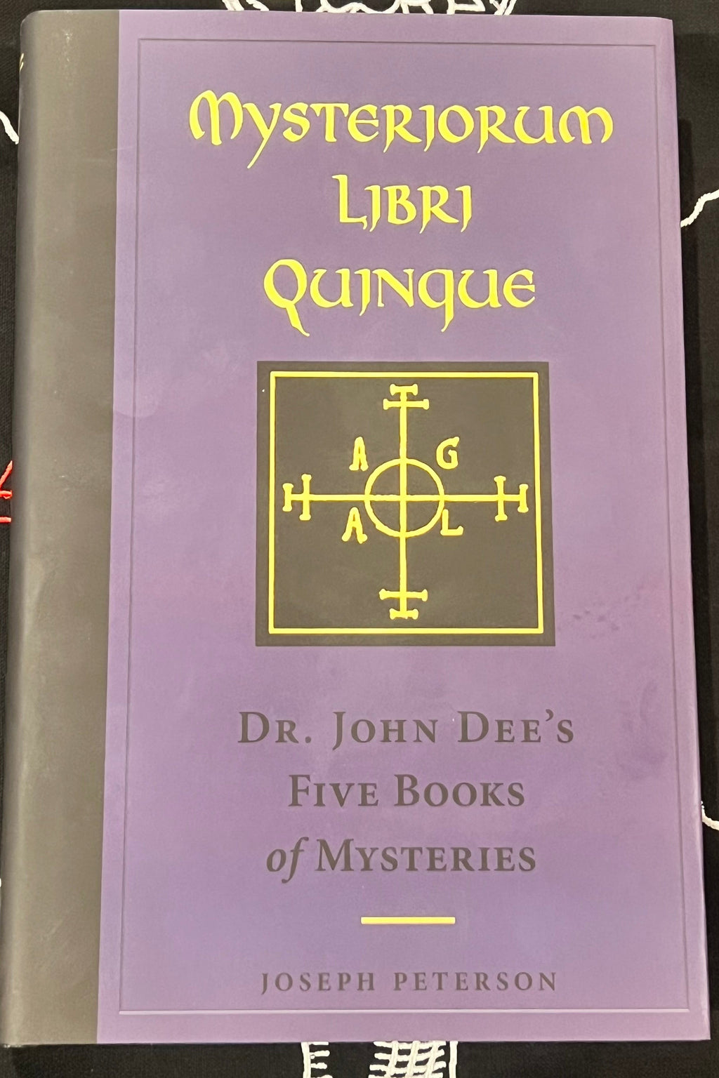 Mysteriorum Libri Quinque book front cover with dust jacket on top of fabric background. 