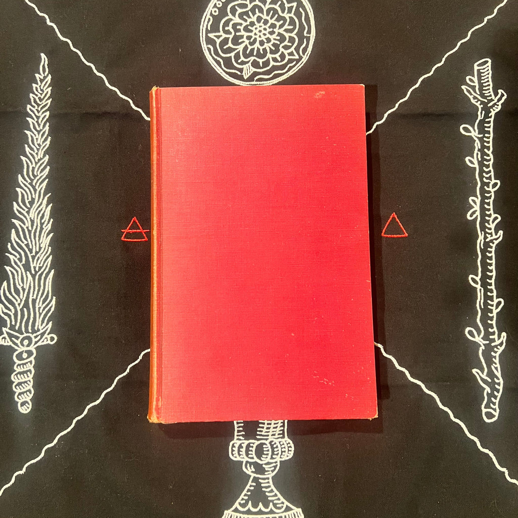 A red hardcover book lies centered on a black background printed with white occult-style illustrations and small red symbols.