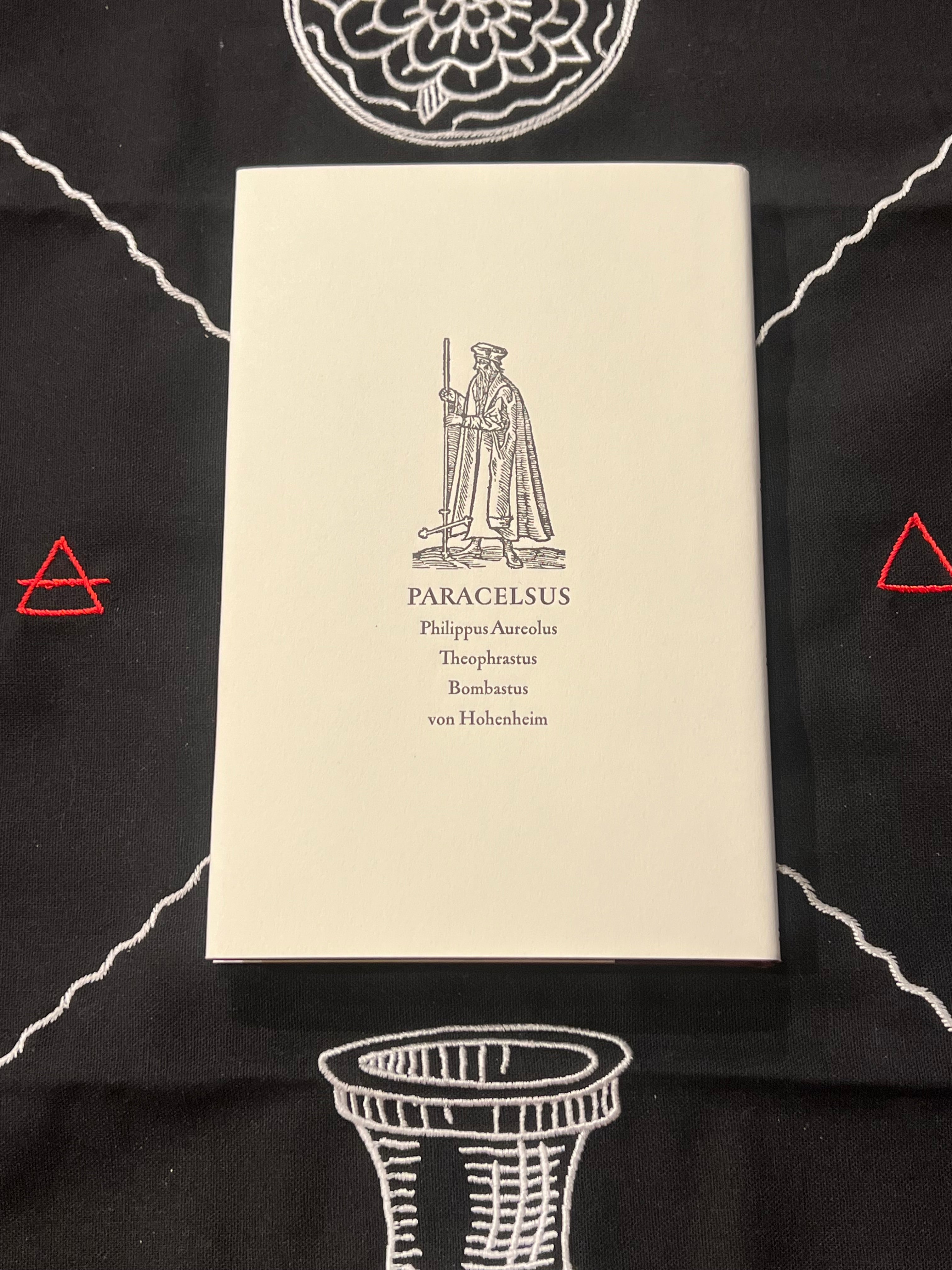 A cream-colored book titled 'PARACELSUS' by Philipp-Antonius Theophrasus Bombastus von Hohenheim, displayed flat on a black fabric background with white and red geometric patterns.
