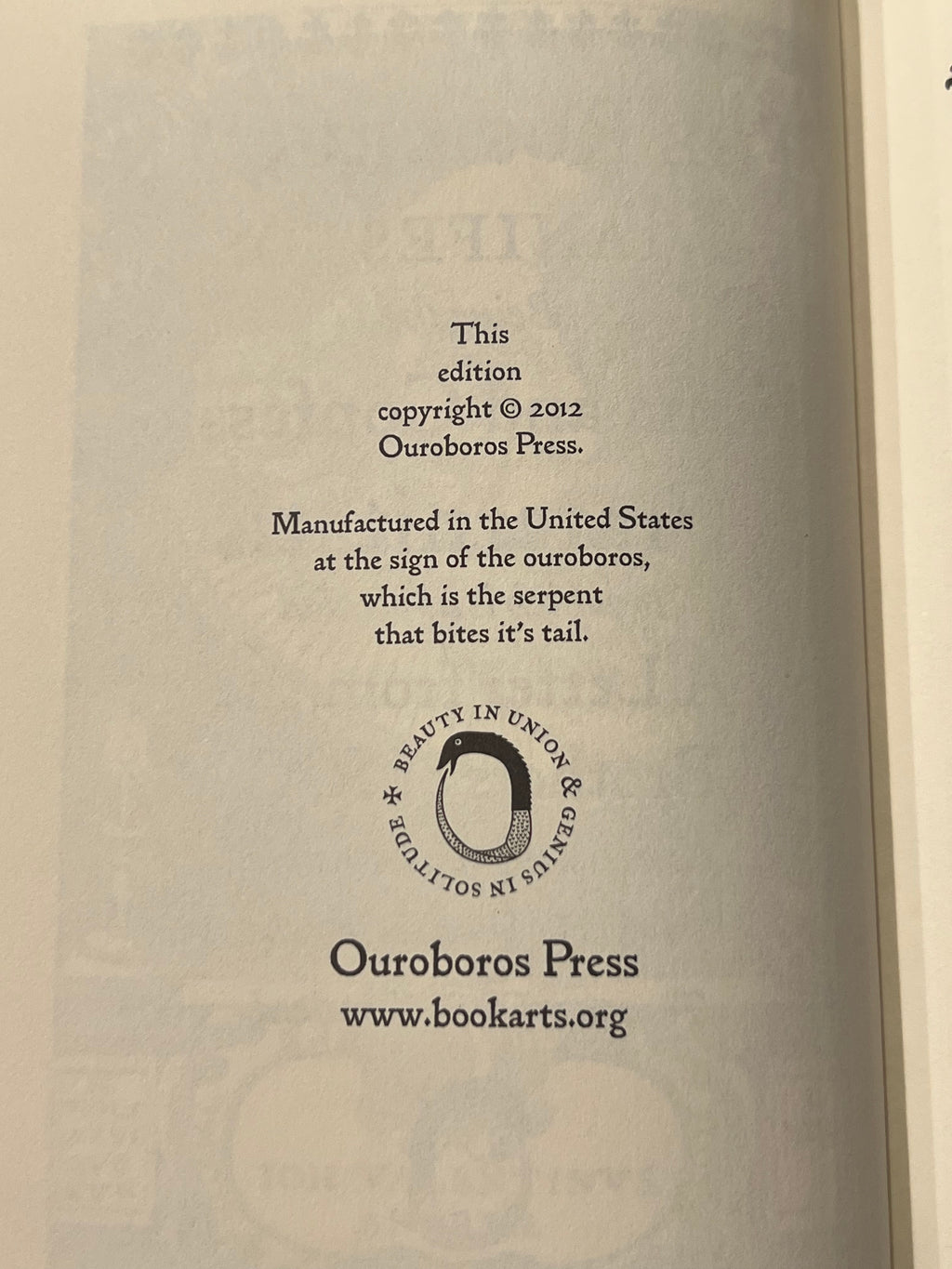 A close-up of an open book's printed interior page showing copyright text for 'This edition' from 2012, the publisher name Ouroboros Press, a circular logo, and the website www.bookarts.