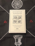 A cream-colored book titled 'Rosicrucian Manifestos' by Ourorbor Press, displayed on a black cloth with white occult-style illustrations and small red triangle accents.