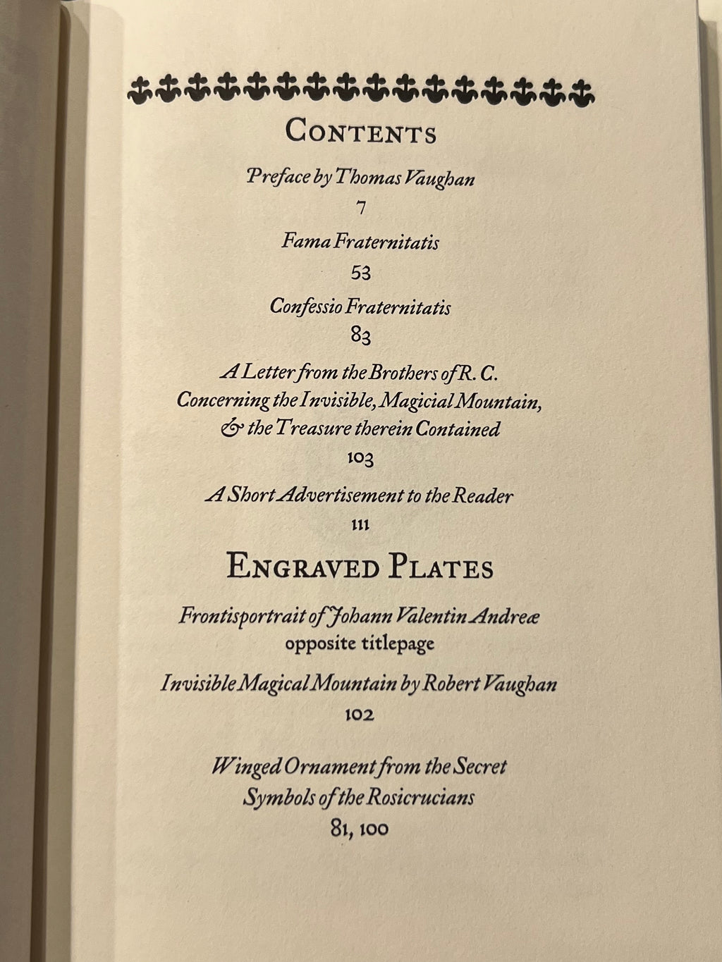 A close-up of an open book's printed table of contents page, showing black text on warm off-white paper with decorative floral motifs at the top.