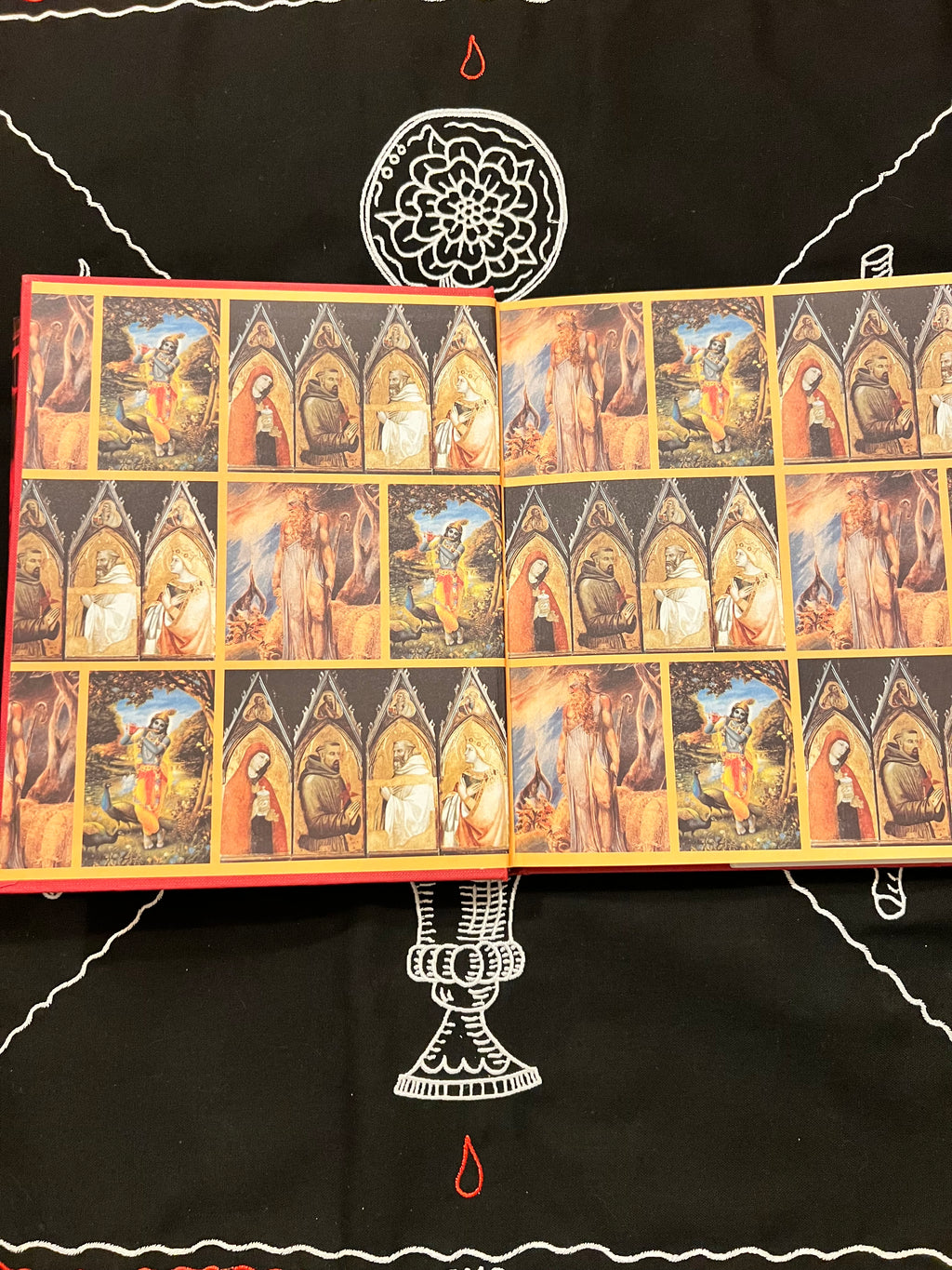 An open art book or album spread, showing multiple small framed-style paintings of figures in arched scenes, placed on a black fabric background with white and red decorative markings.