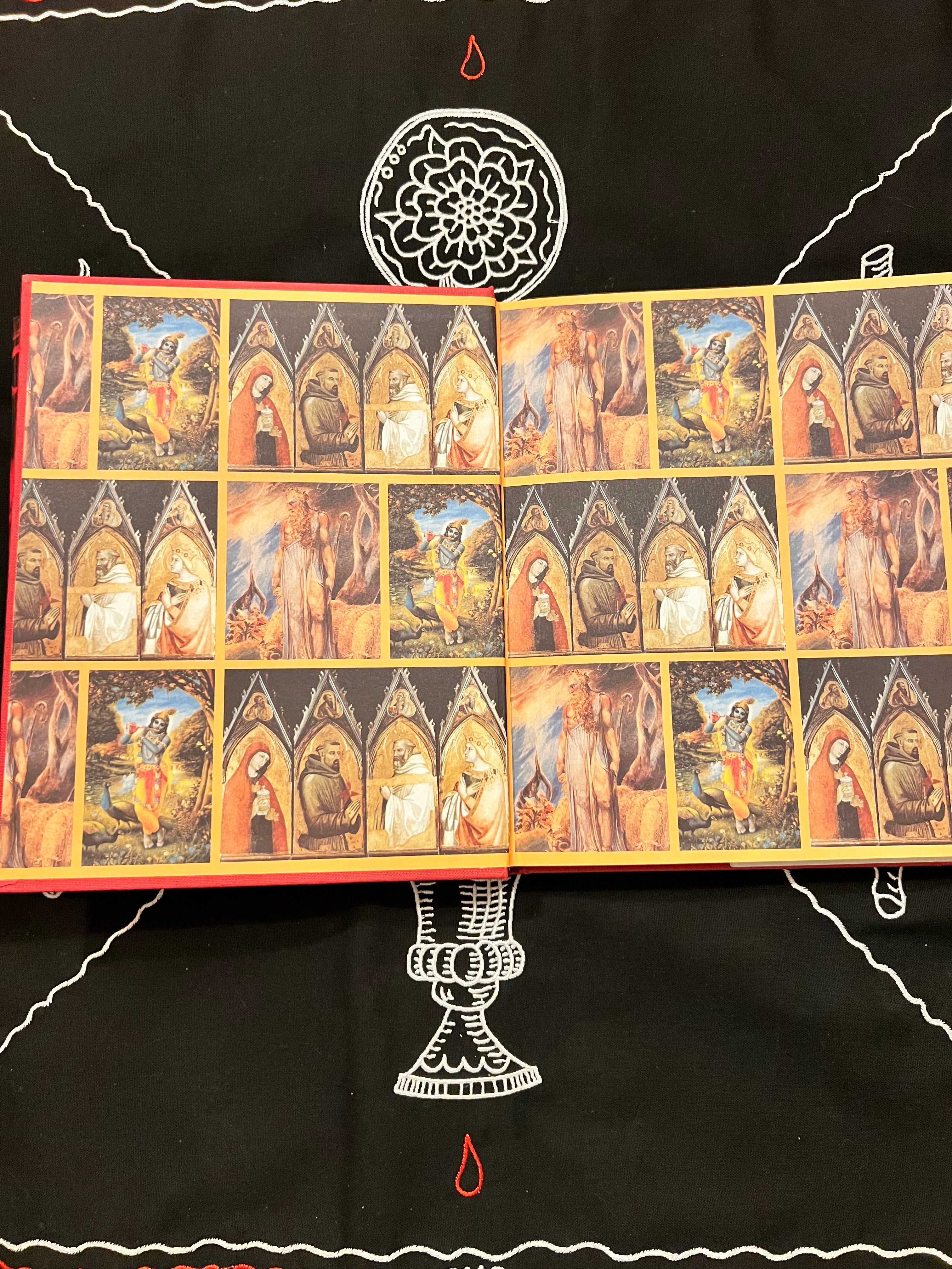 An open art book or album spread, showing multiple small framed-style paintings of figures in arched scenes, placed on a black fabric background with white and red decorative markings.