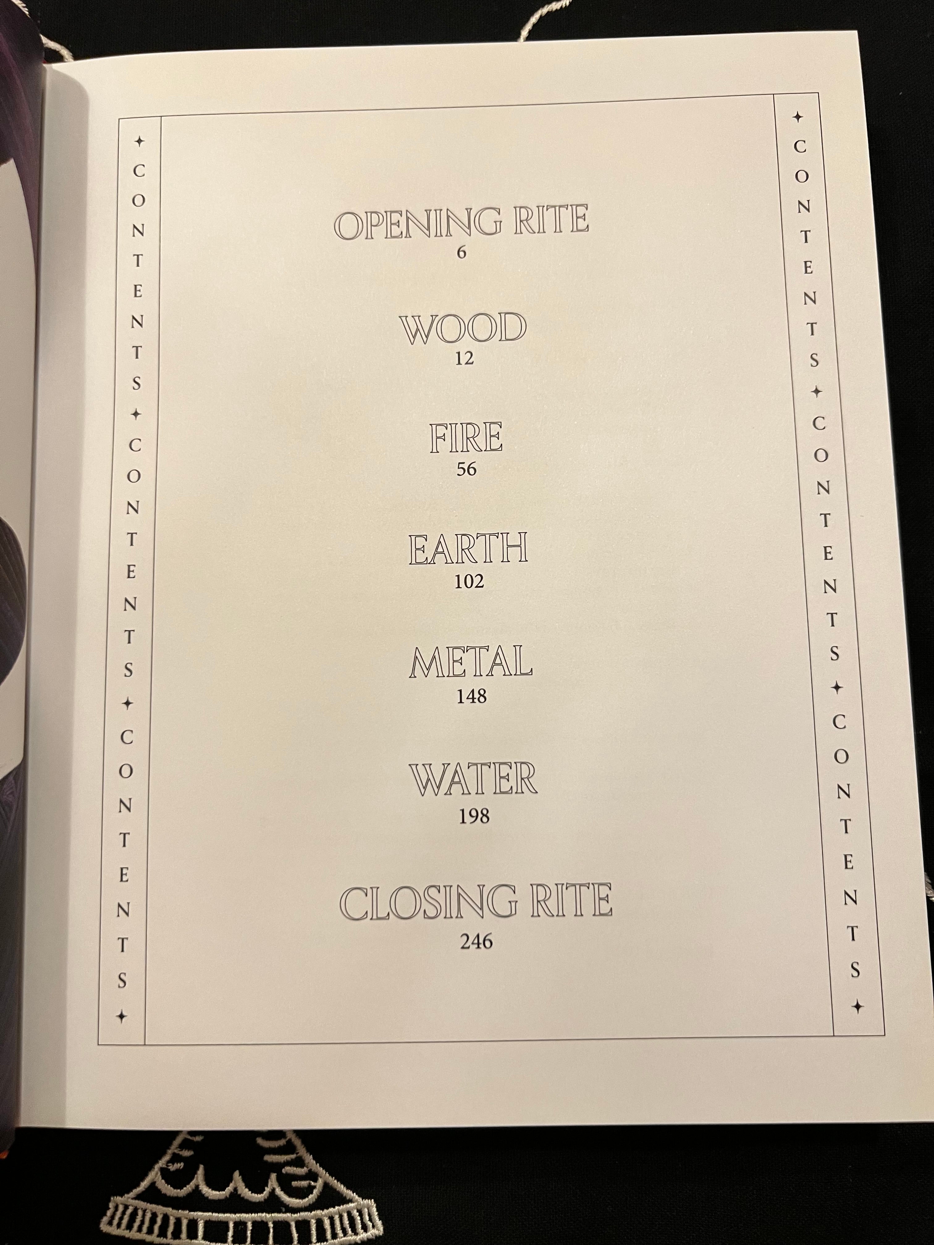 An open book or booklet showing a printed table of contents page with headings such as Opening Rite, Wood, Fire, Earth, Metal, Water, and Closing Rite, photographed against a dark background.