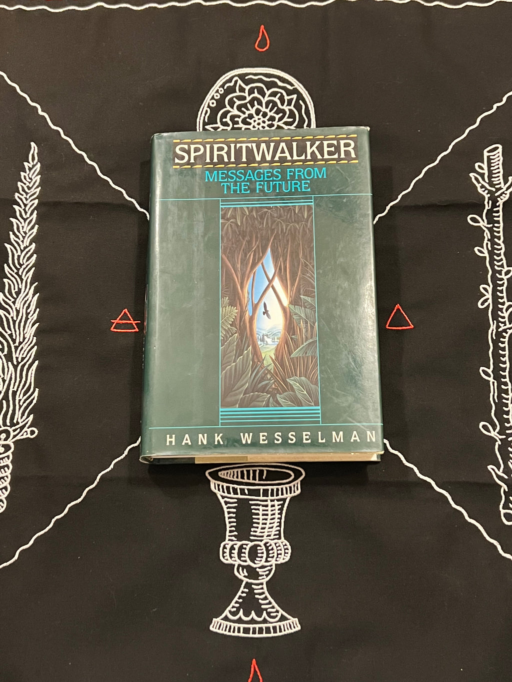 A hardcover book titled 'Spiritwalker: Messages from the Future' by Hank Wesselman, placed on a black cloth with white occult-style illustrations and red symbols.