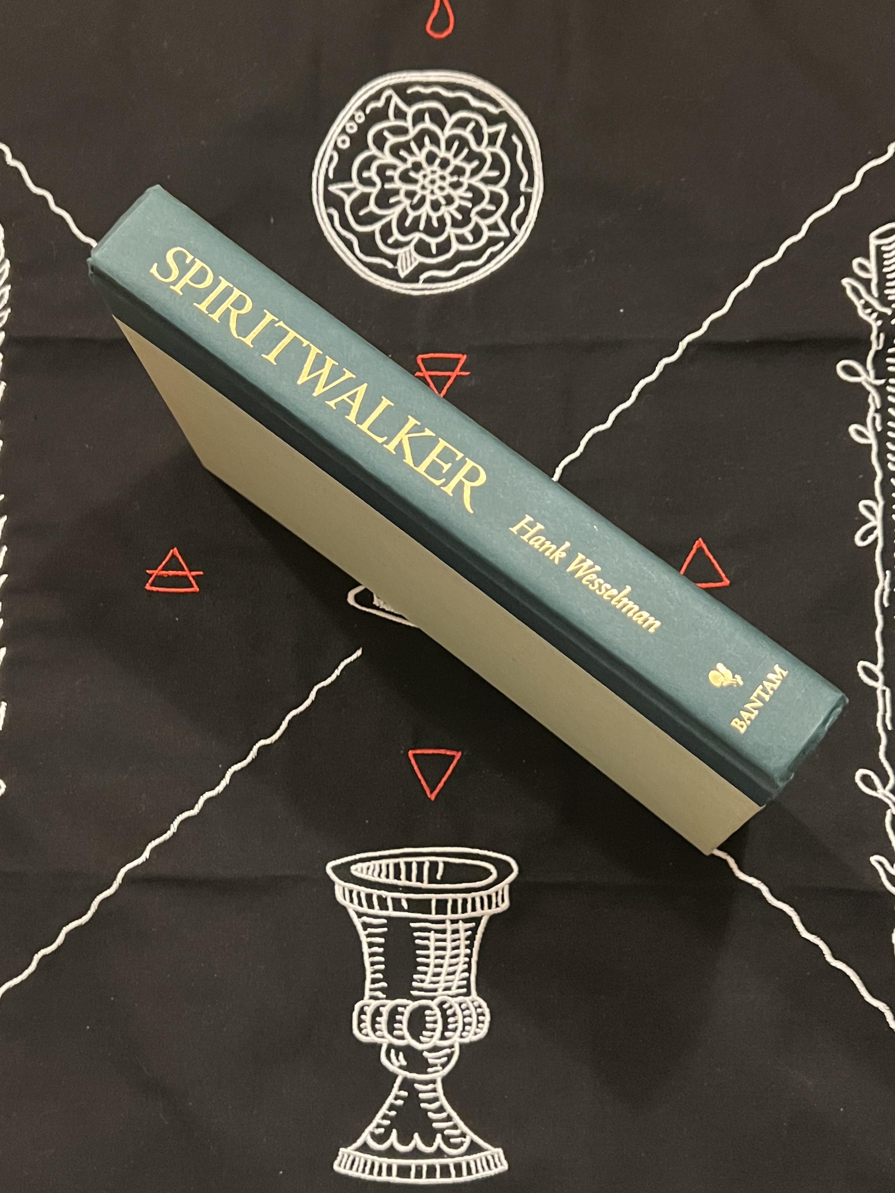 A hardcover book titled 'SPIRITWALKER' by Frank Woodman, published by Bantam, resting diagonally on a black cloth printed with white occult-style illustrations.