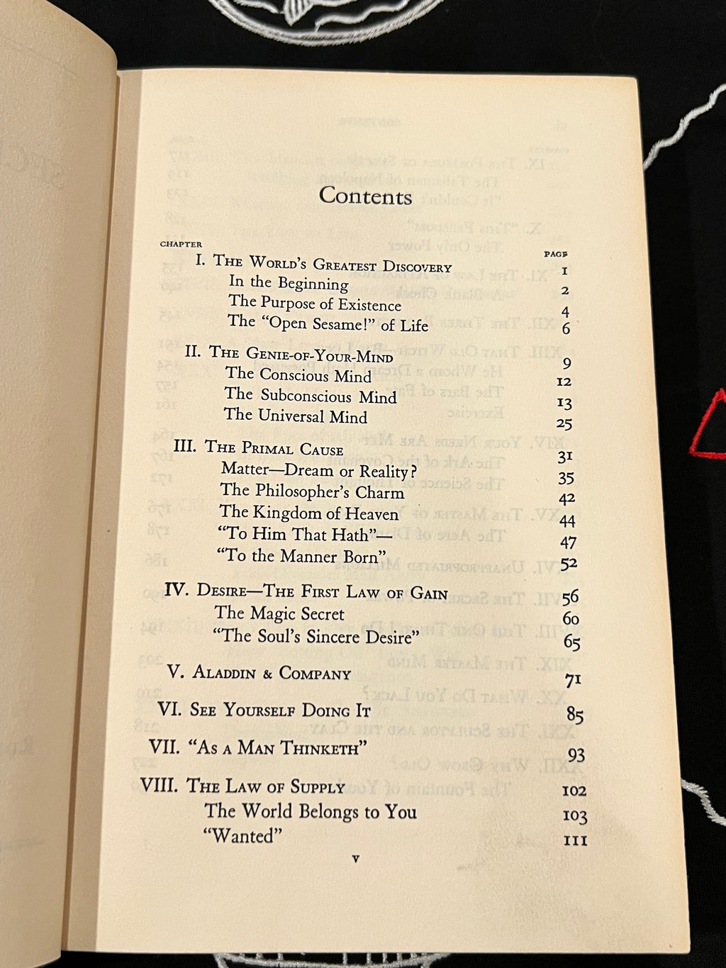 An open book showing the printed Contents page with chapter titles, page numbers, and a table of contents on aged cream paper against a dark background.