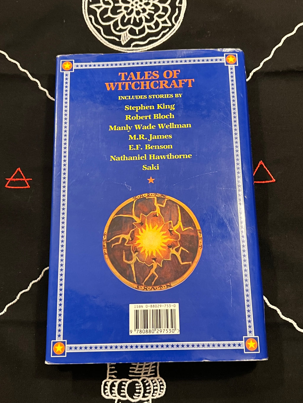 The back cover of the book 'Tales of Witchcraft' featuring a vibrant blue background with a central glowing orange circular emblem, listed on a black cloth background.