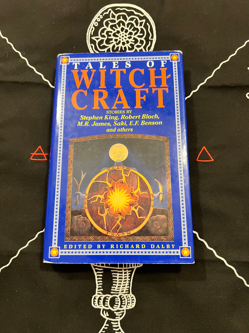 A boxed book titled "Tales of Witch Craft" stands upright on a black cloth with white occult-style line drawings. The box is blue with large orange title text and an illustrated circular mystical design on the front.