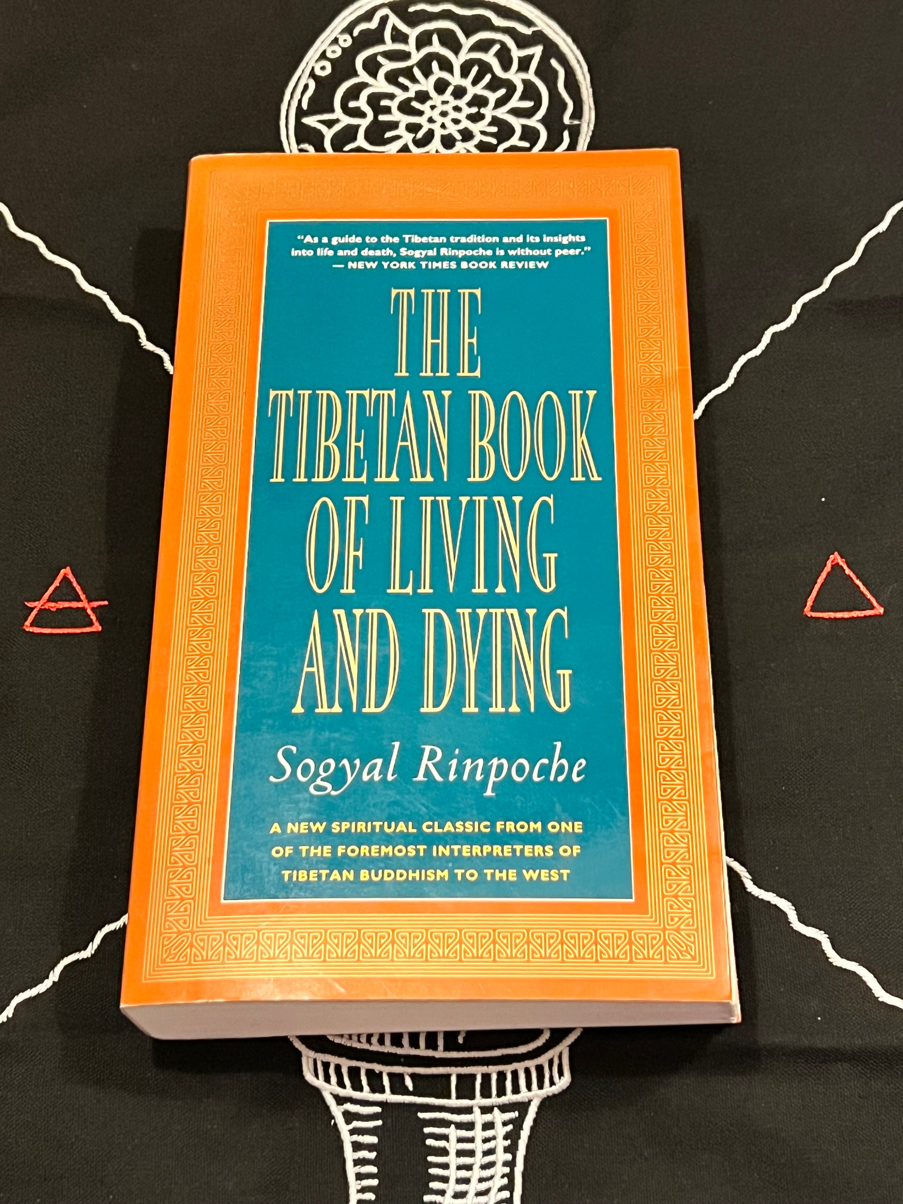 The Tibetan Book of Living and Dying by Soyyal Rinpoche, featuring a bright orange cover with a teal-blue central panel and gold lettering, displayed on a black background with white and red geometric designs.